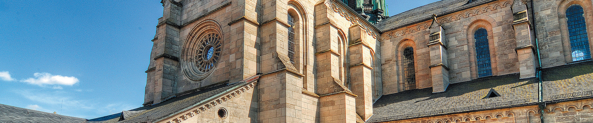 Blick aus dem Abteigarten auf die frühgotische Klosterkirche Ebrach aus fränkischem Sandstein, deren dunkelgrüner Turmhelm mit goldener Spitze in den Himmel ragt.